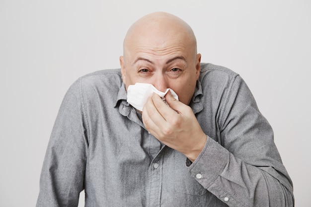 Sick bald middle-aged guy sneezing in napkin