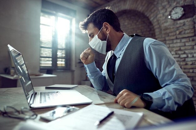 Больной бизнесмен в маске и кашляет во время работы за компьютером в офисе