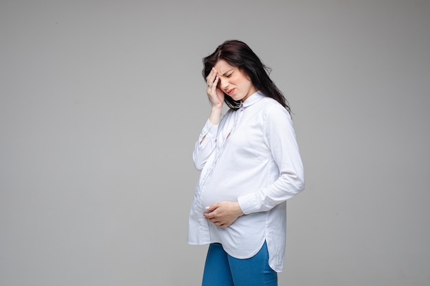 Sick caucasian pregnant female touches her head because of a strong headache
