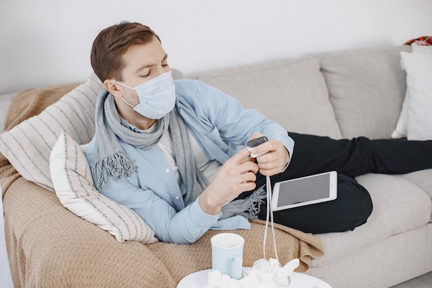 거실에서 아픈 사람입니다. 중년 남성은 집에서 감기와 발열로 몸살을 앓고 있습니다. 의료용 마스크를 쓴 남자.