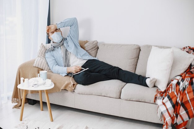 Sick guy in living room. Middle age man feeling sick with cold and fever at home. Man in a medical mask.