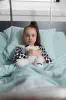 Free photo sick little girl under treatment wearing oxygen tube while holding plush bear toy. ill kid resting in children healthcare facility patient bed alone while having teddy bear.