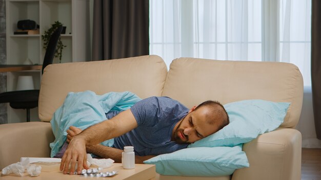 Sick man lying on sofa covered with blanket during global pandemic.