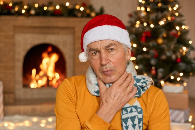 Sick man in orange sweater, scarf and Christmas hat suffering from sore throat