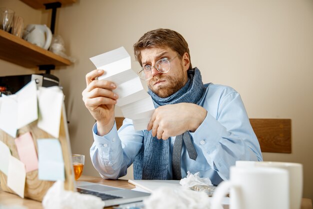 Sick man reading prescription medicine working in office, businessman caught cold, seasonal flu. Pandemic influenza, disease prevention, illness, virus, infection, temperature, fever and flu concept