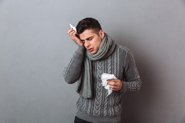 Sick Man in sweater and scarf with serviette and spray having headache