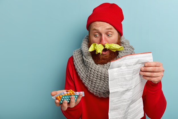 Sick man in warm clothes with paper tissues and pills