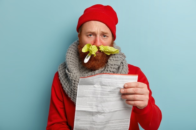 Sick man in warm clothes with paper tissues and thermometer