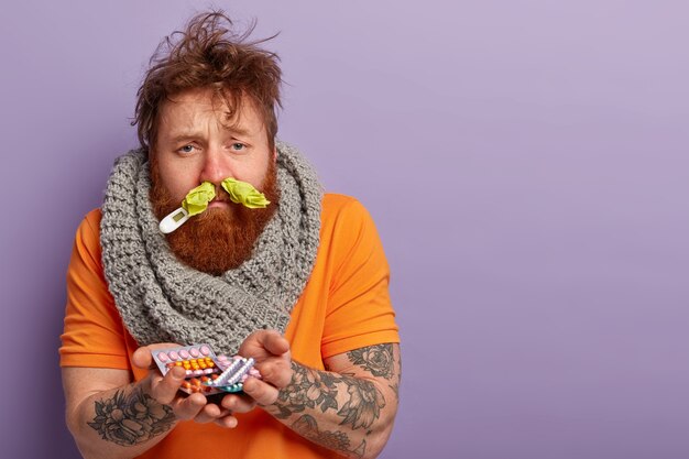 Sick man in warm clothes with thermometer and pills