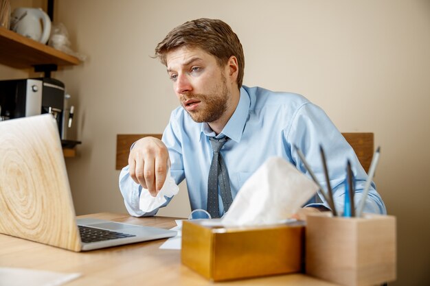 Больной человек с носовым платком чихает и сморкается во время работы в офисе, бизнесмен простудился, сезонный грипп