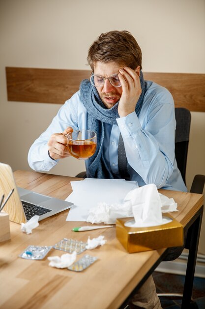 Sick man with handkerchief sneezing blowing nose while working in office