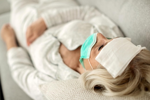 発熱と自宅で横になっているフェイスマスクを持つ病気の成熟した女性