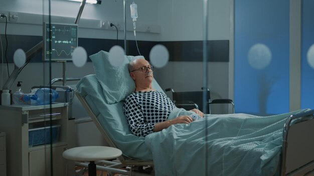 呼吸障害のために鼻酸素チューブを備えた医療施設の病棟のベッドで眠っている病気の患者。病気から回復するための治療を待っている病気の老人