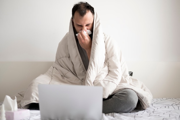 Free photo sick person staying in bed and using his laptop