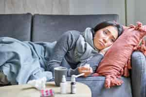 無料写真 病気の悲しい韓国人女性がソファに横たわって気分が悪く、風邪を引いて気分が悪くなり、温度が動揺している