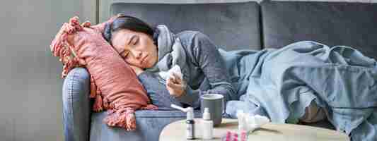 Free photo sick sad korean woman lying on sofa feeling unwell catching cold flu and temperature looking upset