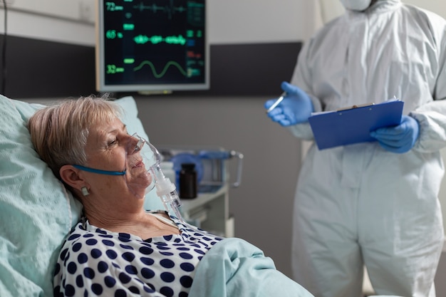 Sick senior woman inhale and exhale through oxygen mask