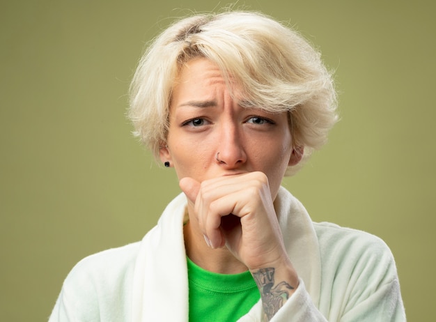 Sick unhealthy woman with short hair feeling unwell coughing standing over light wall