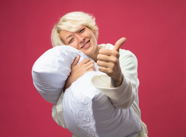 Free photo sick unhealthy woman with short hair hugging pillow feeling better looking  smiling showing thumbs up standing over pink wall