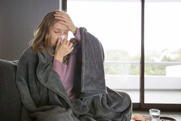 Sick woman blowing nose with napkin, holding hand on head