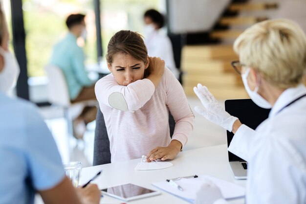 Sick woman coughing into elbow while having appointment with a doctor at the clinic