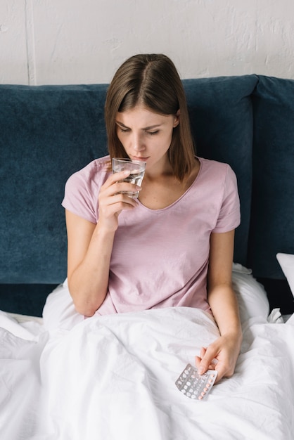 Sick woman drinking water while taking birth control pills