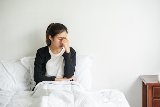 The sick woman had a headache and put her hand on her nose on the bed.