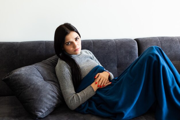 Sick woman, ill young unhealthy girl pain lying at home on sofa couch