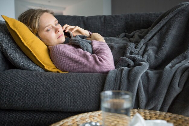 電話で夫を呼び出す、自宅のソファーに横になっている病気の女性