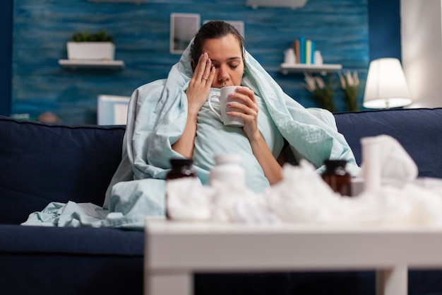 Sick woman sitting at home in blanket with hot tea