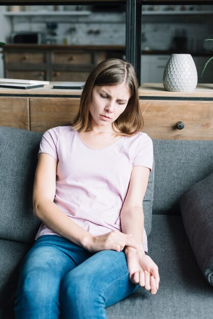 Sick woman sitting on sofa checking her pulse