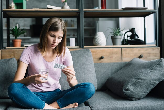 Sick woman sitting on sofa with glass of water and pills