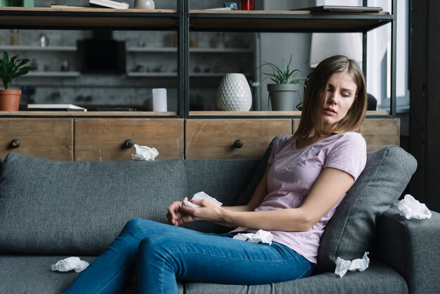 Sick woman sitting on sofa with many crumpled tissue paper around her