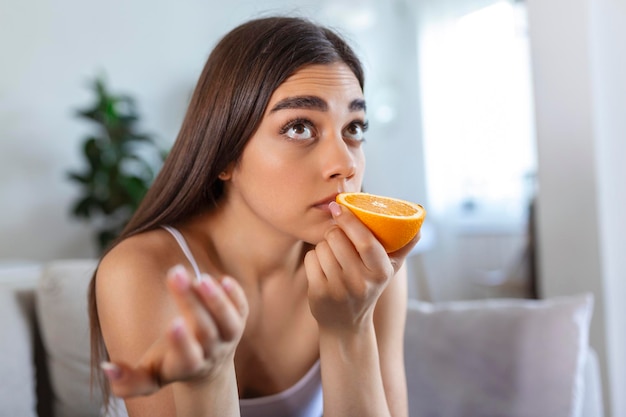 Sick woman trying to sense smell of half fresh orange has symptoms of Covid19 corona virus infection loss of smell and taste One of the main signs of the disease