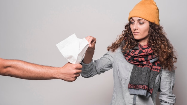 Sick woman wearing scarf around her neck holding tissue paper against gray background
