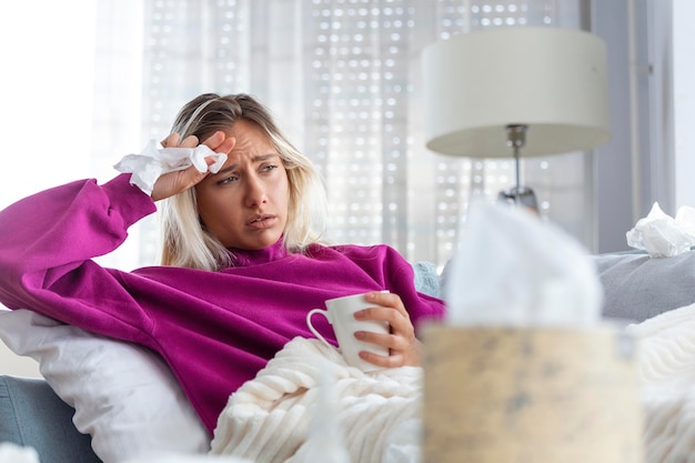 Sick woman with headache sitting under the blanket Sick woman with seasonal infections flu allergy lying in bed Sick woman covered with a blanket lying in bed with high fever Coronavirus symptoms