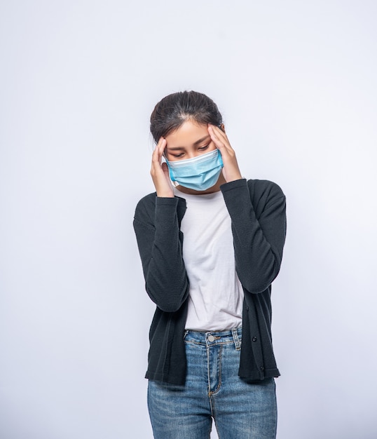 A sick woman with a headache wore a mask and placed a hand on her head.