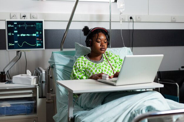 Sick young patient with headphones using laptop