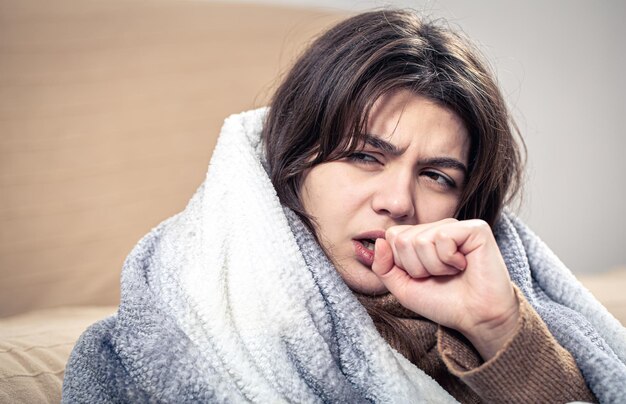 A sick young woman is coughing wrapped in a blanket