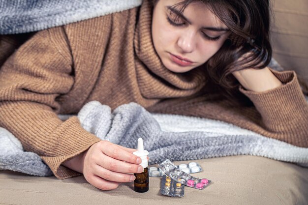 Sick young woman with medicines lies in bed colds and home treatment