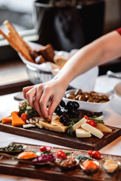 Sidce view of various types of cheese with nuts grapes and honey on wooden platter