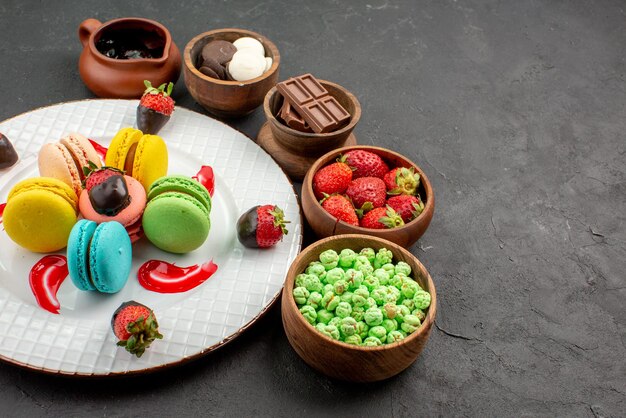 Side close-up French macaroon French macaroons chocolate-covered strawberries and sauce and five bowls of sweets on the table