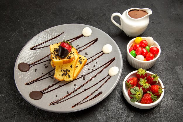 Side close-up view appetizing cake grey plate of cake with chocolate-covered strawberries and chocolate sauce in bowls