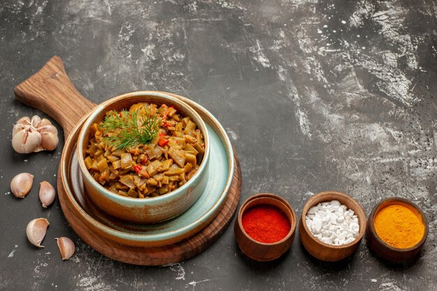 にんにくの横にあるスパイスの食欲をそそる皿ボウルと黒いテーブルのまな板に食欲をそそるインゲンとトマトの側面のクローズアップビュー