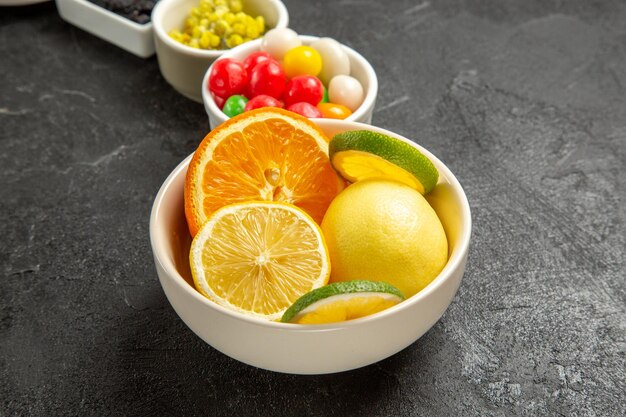 Side close-up view appetizing fruits and berries white bowls of citrus fruits and candies on the black table