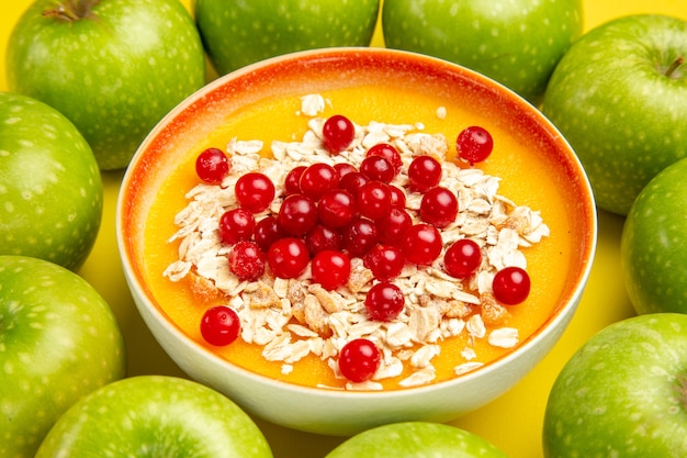 Side close-up view apples the appetizing apples around bowl of red currants oatmeal on the table