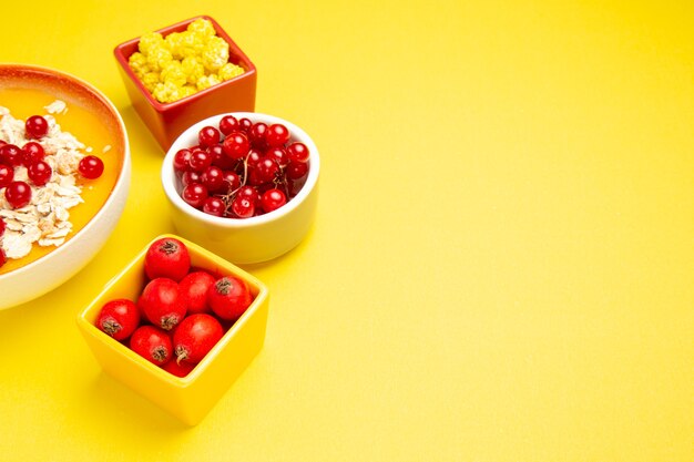 Вид сбоку крупным планом ягоды, ягоды, овсяные хлопья, желтые конфеты в мисках