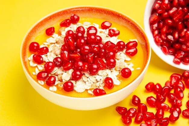 Side close-up view berries orange plate of oatmeal pomegranate seeds and red currants