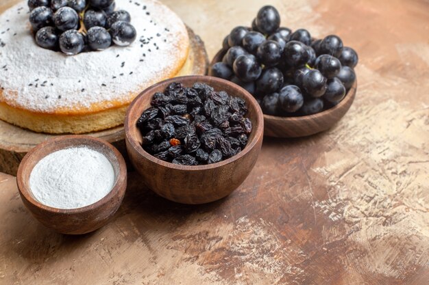 Side close-up view a cake an appetizing cake on the board bowls of grapes sugar raisins