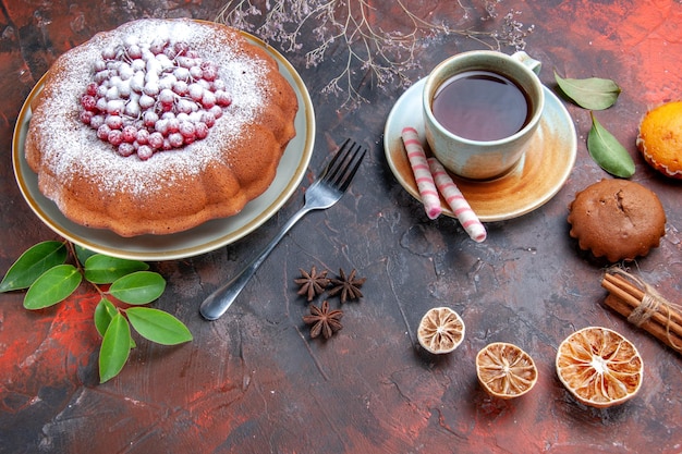 Side close-up view a cake a cake with berries cinnamon sticks cupcakes a cup of tea citrus fruits